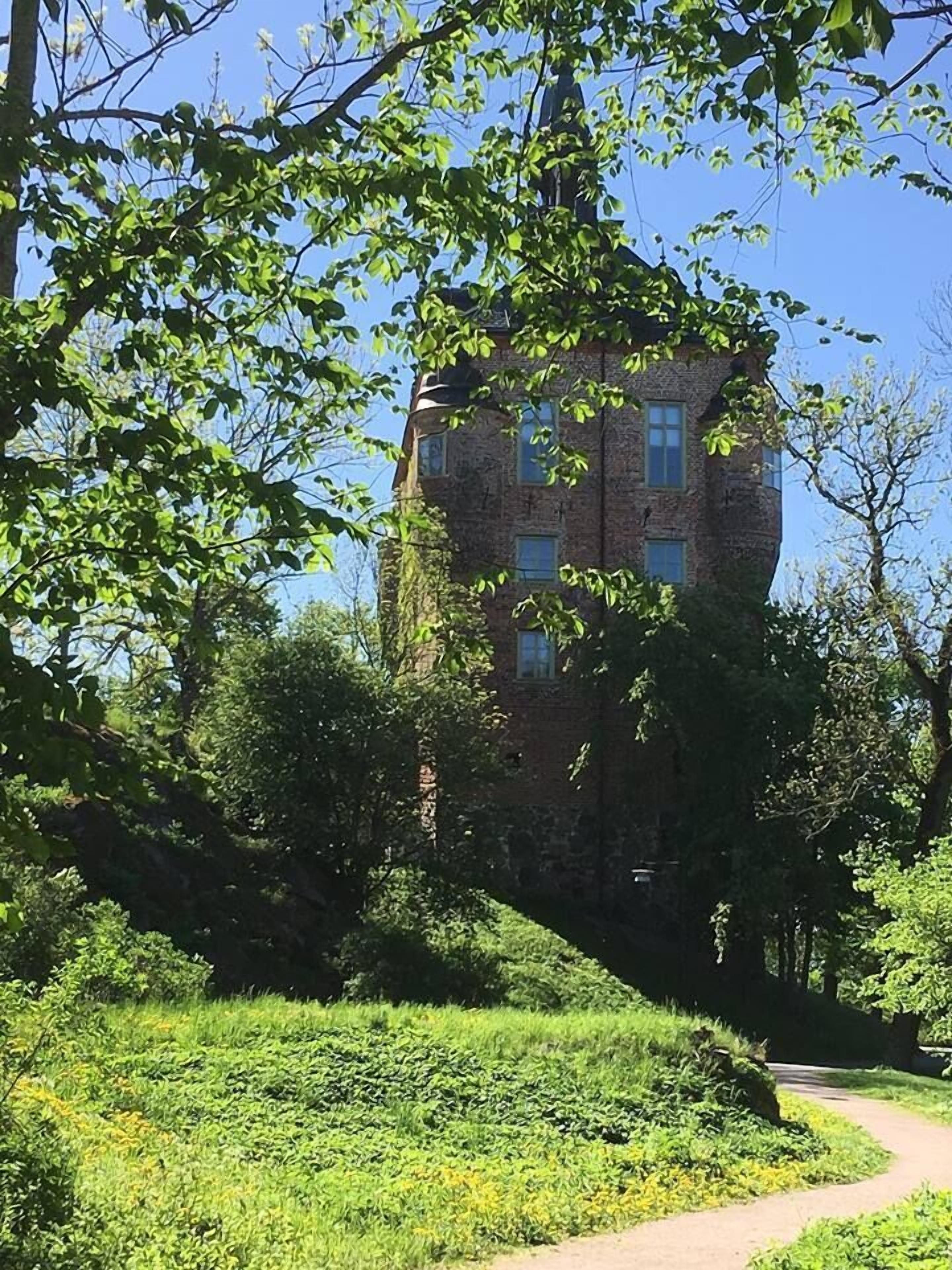 Ein Backsteinhaus mit vielen Fenstern, umgeben von üppigem Grün und Bäumen.