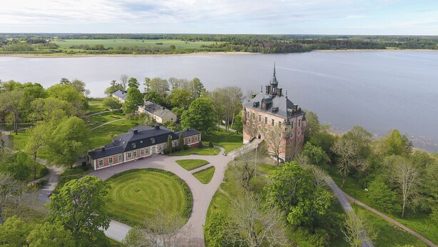 Ein großes, historisches Gebäude mit einem markanten Turm, umgeben von üppiger Vegetation und einem See.