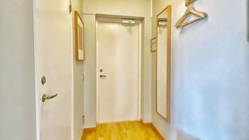 A hallway with a wooden floor, a bench, a drying rack, and a door at the end.
