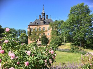 A large brick building with a clock tower, surrounded by lush gardens and flowering plants.