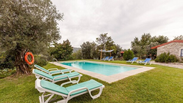 Une piscine avec des chaises longues, une bouée de sauvetage et un bâtiment en pierre en arrière-plan.