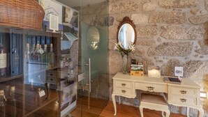 Une pièce avec un mur en pierre, une porte en verre donnant sur une piscine, une coiffeuse blanche avec un miroir et un panier en osier.