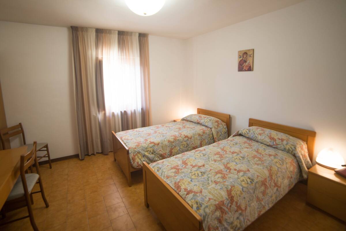 Ein Zimmer mit zwei Einzelbetten, einem Holztisch und einem Stuhl.