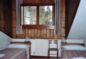 Une chambre avec deux lits, un radiateur, une fenêtre avec des rideaux et une chaise.