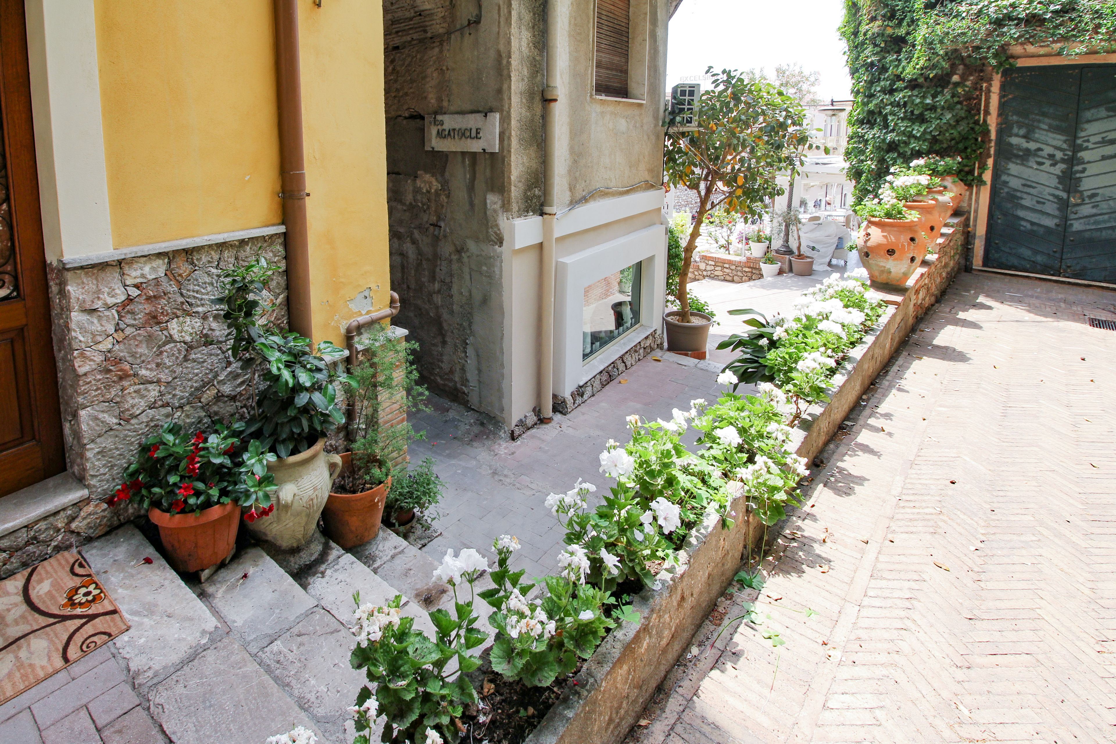 A courtyard with potted plants, a stone wall, and a tiled floor.