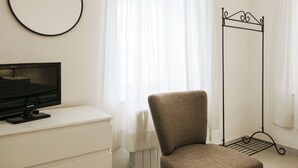 Une chambre à coucher comprenant un lit, une table de chevet, un téléviseur, une chaise, une armoire, un miroir et une fenêtre avec des rideaux.