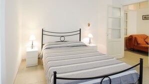 Un lit bien fait, recouvert d’une couvre-lit à rayures, avec deux lampes de chevet et une table de chevet blanche.