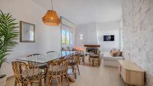 Ett modernt vardagsrum med ett glasbord, flätade stolar, en vit soffa och en vägg av sten.