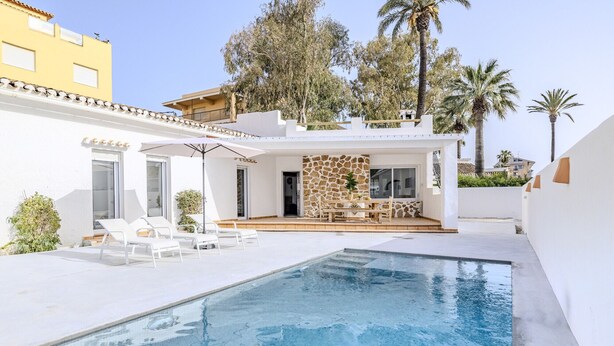 En swimmingpool med solstolar, en stenmur och en uteplats.