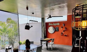 Een modern interieur met een ronde tafel, stoelen, een plafondventilator, hanglampen en een muur met een klok en decoratieve objecten.