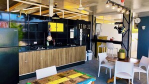 A modern kitchen with a wooden countertop, a black backsplash, and a black refrigerator. There are white chairs and a table with a colorful table runner.