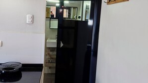 A kitchen with a black refrigerator, a sink, and a countertop. There is a wooden rack with hooks on the wall.