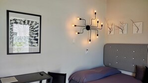 A bedroom with a bed, a desk, and a wall-mounted light fixture.