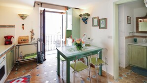 A dining area with a green table and chairs, a kitchen with a sink and cabinets, and a balcony with a view. - Corso Umberto (Taormina)
