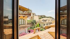 A view from a window overlooking a residential area with terracotta-roofed buildings, balconies, and a hillside in the background. - Corso Umberto (Taormina)