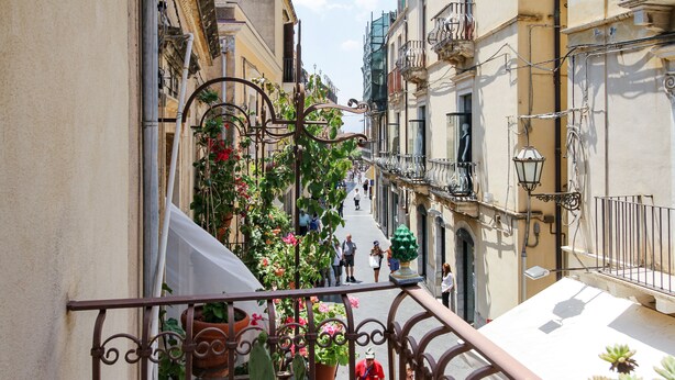 A narrow street with balconies, potted plants, and pedestrians. - Corso Umberto (Taormina)