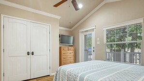 A bedroom with a large bed, a wooden dresser, a television on a stand, and a window with blinds. - Sunset View at CrossTimbers Marina (Sperry)