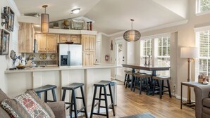 A spacious kitchen with wooden cabinets, a central island with stools, and a dining area with a table and chairs. - Sunset View at CrossTimbers Marina (Sperry)
