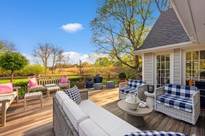 Eine Holzterrasse mit Gartenmöbeln, einem kleinen Tisch und Blick auf ein Wiesenfeld.