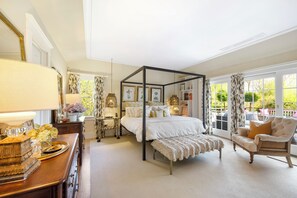 A bedroom with a four-poster bed, a wooden dresser, a chair, and a large window with curtains. - Southampton Village So of Hwy; water View PREMIER HOST (Southampton)