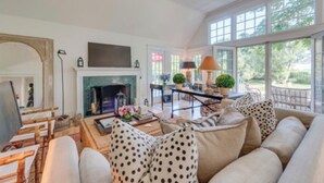 A spacious living room with a fireplace, comfortable seating, and large windows offering a view of the outdoors. - Southampton Village So of Hwy; water View PREMIER HOST (Southampton)