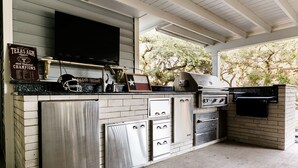 A covered outdoor kitchen with a TV, grill, and Texas A&M memorabilia. - Beautiful Country Home Minutes from Magnolia & Baylor Pool HotTub River Front (Crawford)