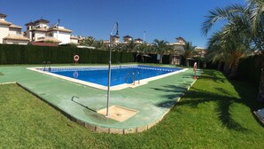 A rectangular swimming pool with two ladders, surrounded by a green lawn and palm trees. - Villa with pool 7 minutes from the beach walking. WIFI + Air Conditioning (La Marina del Pinet)