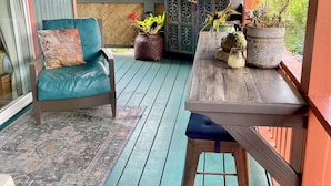 Een veranda met een blauwe fauteuil, een houten tafel met potplanten en een decor kast.