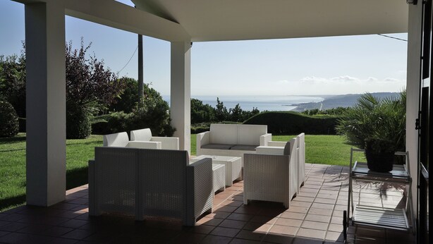 Un patio cubierto con mobiliario de mimbre blanco y vista al mar.