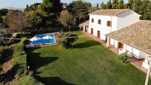 Una casa grande de color blanco con piscina, rodeada de exuberante vegetación y árboles.