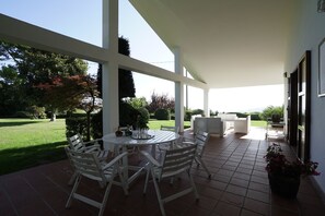 A covered patio with a round table and chairs, a sofa, and potted plants.