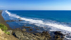 Un paisaje costero con una costa rocosa, océano azul y una línea de costa distante con vegetación.