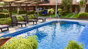Una piscina con sillones de descanso y una zona cubierta, rodeada de jardines bien cuidados.