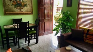 Una sala de estar con comedor, un cuadro grande, una planta en maceta y un sofá con cojín.