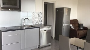 Una cocina moderna con electrodomésticos de acero inoxidable, lavavajillas y una zona de comedor con una silla de cuero marrón.