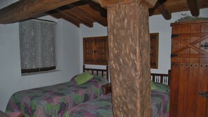 Une chambre avec deux lits, des poutres en bois, une fenêtre avec un rideau et une armoire en bois.