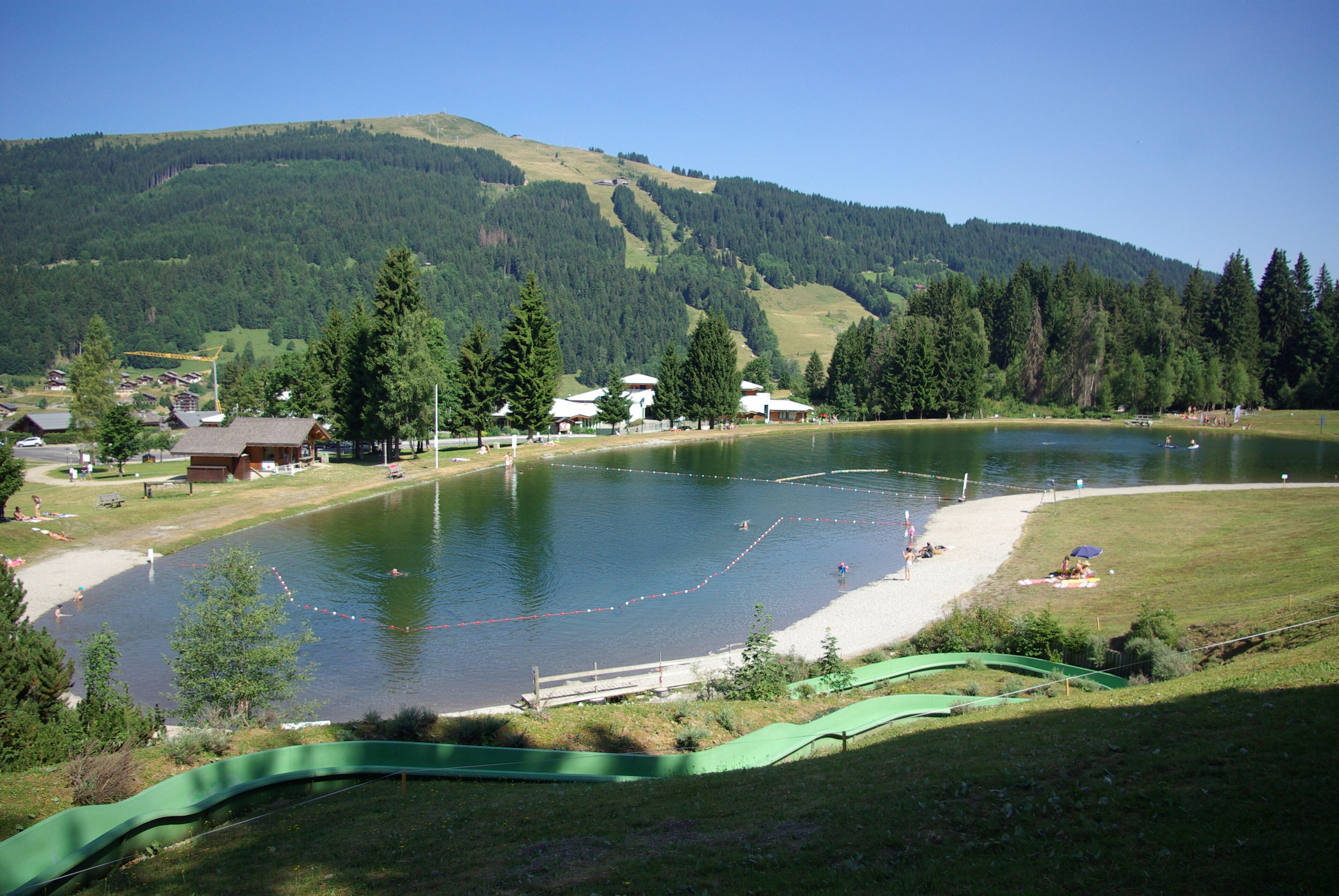 Un resort frente al lago con zona para nadar, un pequeño muelle y vistas a una montaña boscosa.