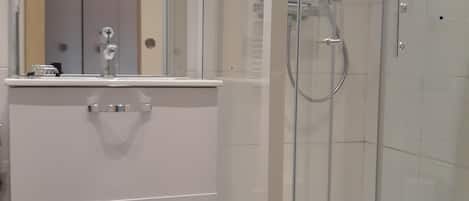 Un baño con cabina de ducha de vidrio, tocador blanco con cajones y un espejo.
