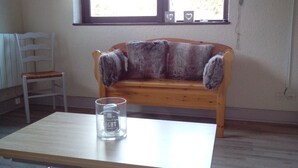 A room with a wooden bench, a white chair, and a glass table with a can.