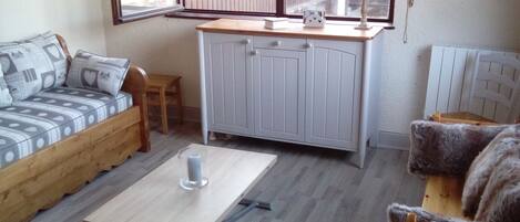 Een gezellige kamer met een houten bank, een tafeltje met een kaars, een kast en een fauteuil met een bont vest.