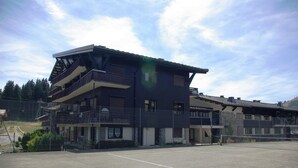 A multi-story building with balconies, a tennis court, and a mountainous backdrop.