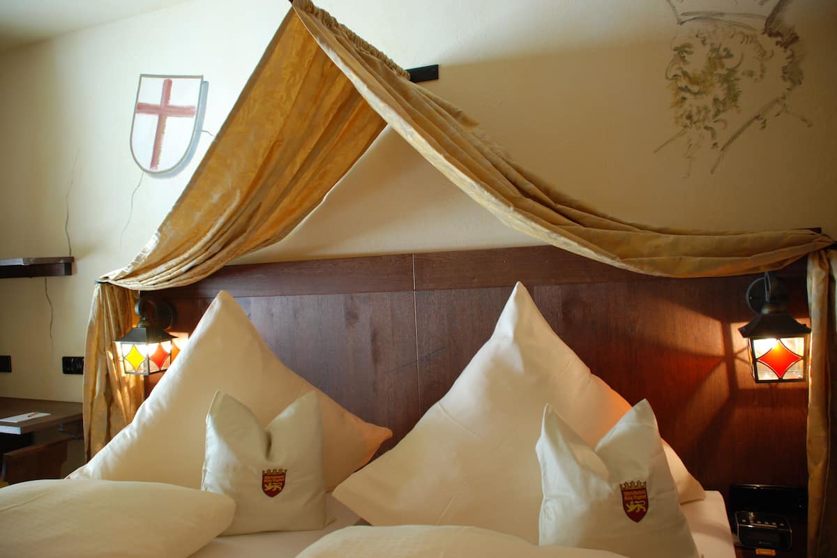 A hotel room with a canopy bed, a wooden headboard, and a shield emblem on the wall.