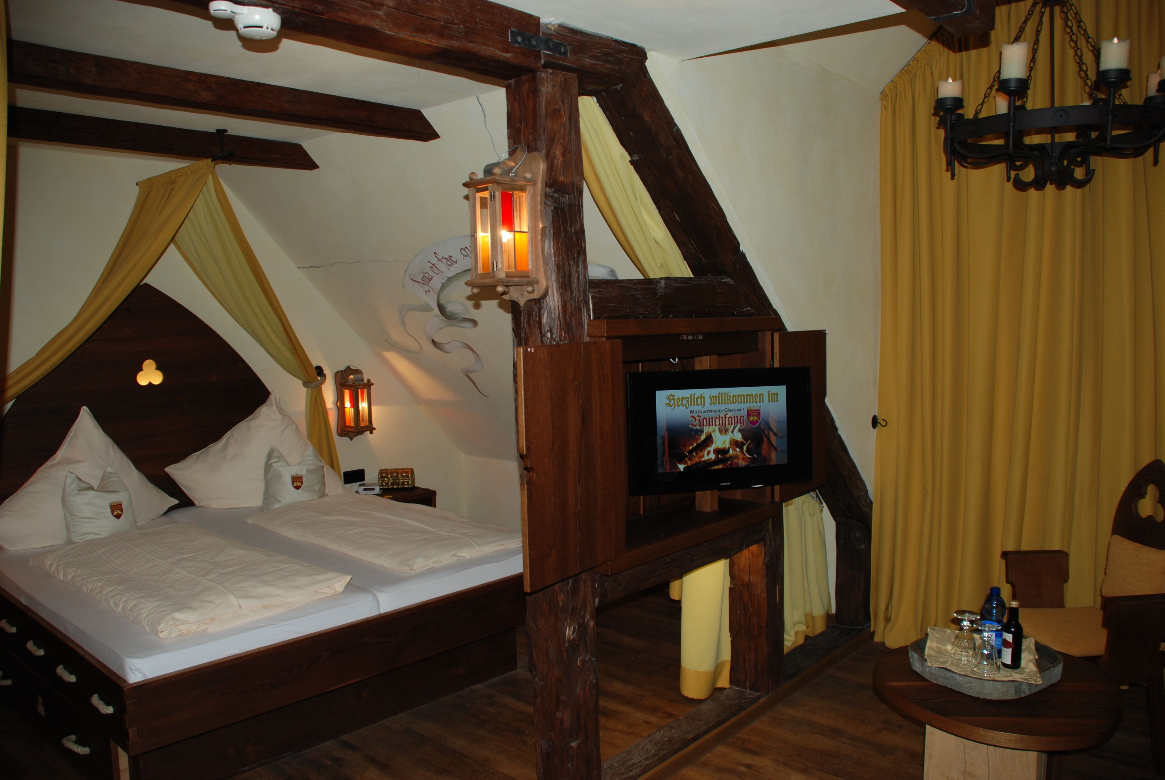 Ein traditionell eingerichteter Raum mit einem hölzernen Bett, einem an der Wand befestigten Fernseher und einer Kandelaberleuchte.