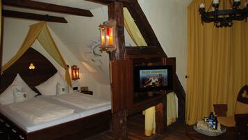 Ein traditionell eingerichteter Raum mit einem hölzernen Bett, einem an der Wand befestigten Fernseher und einer Kandelaberleuchte.