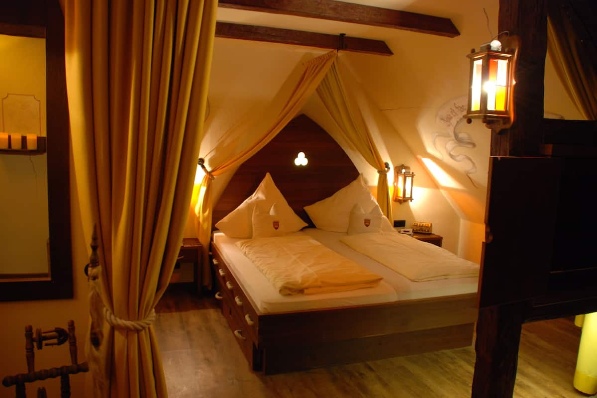 A bedroom with a canopy bed, wooden headboard, bedside lamps, and a wall-mounted light fixture.