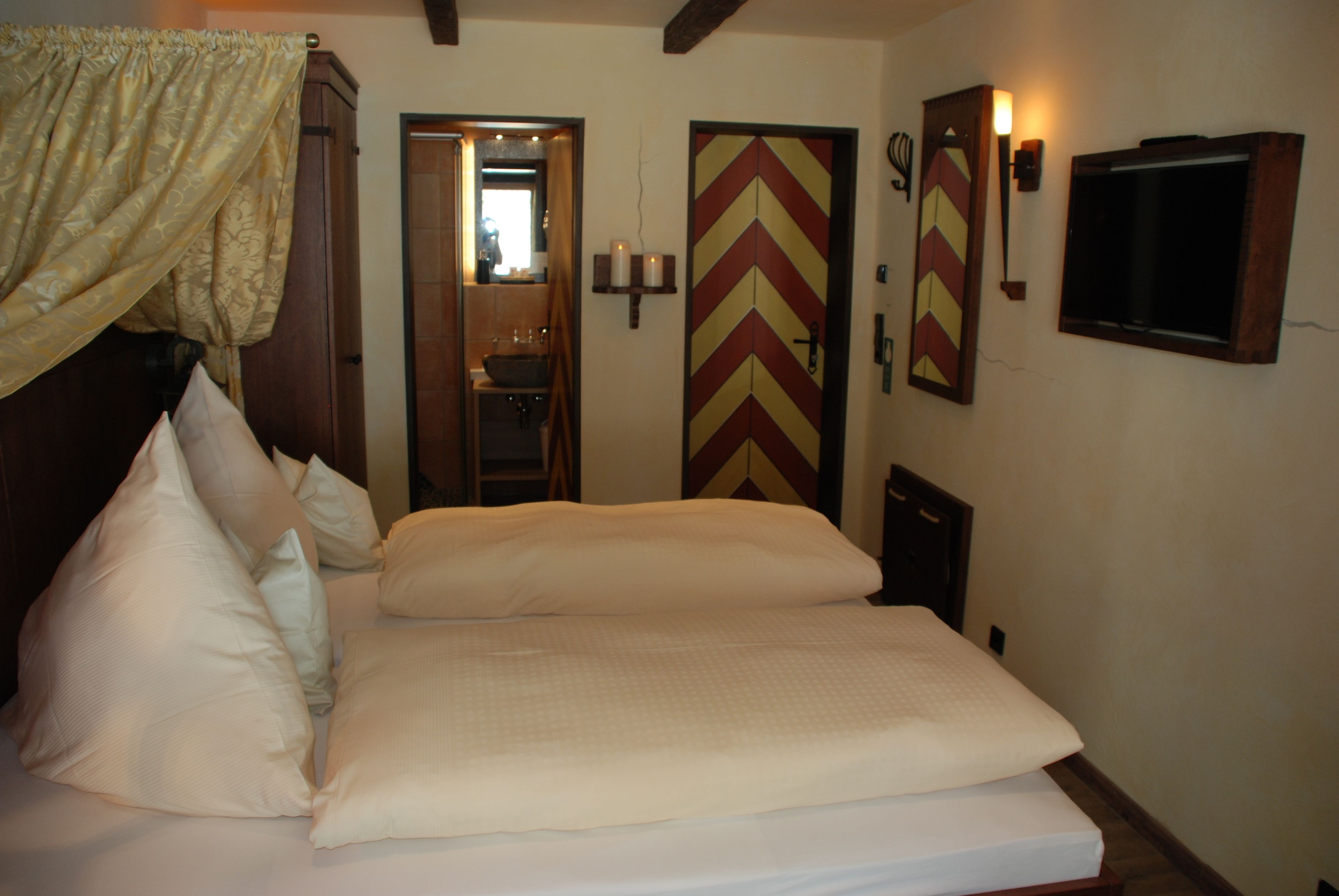 A neatly made bed with pillows, a mirror, a wall-mounted TV, and a chevron-patterned door.