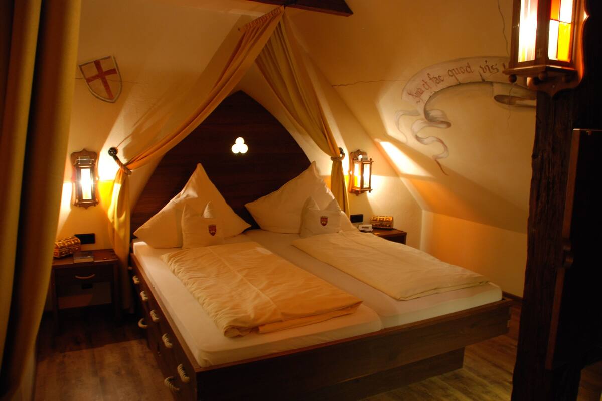 A bedroom with a canopy bed, wooden headboard, and two bedside tables with lamps.