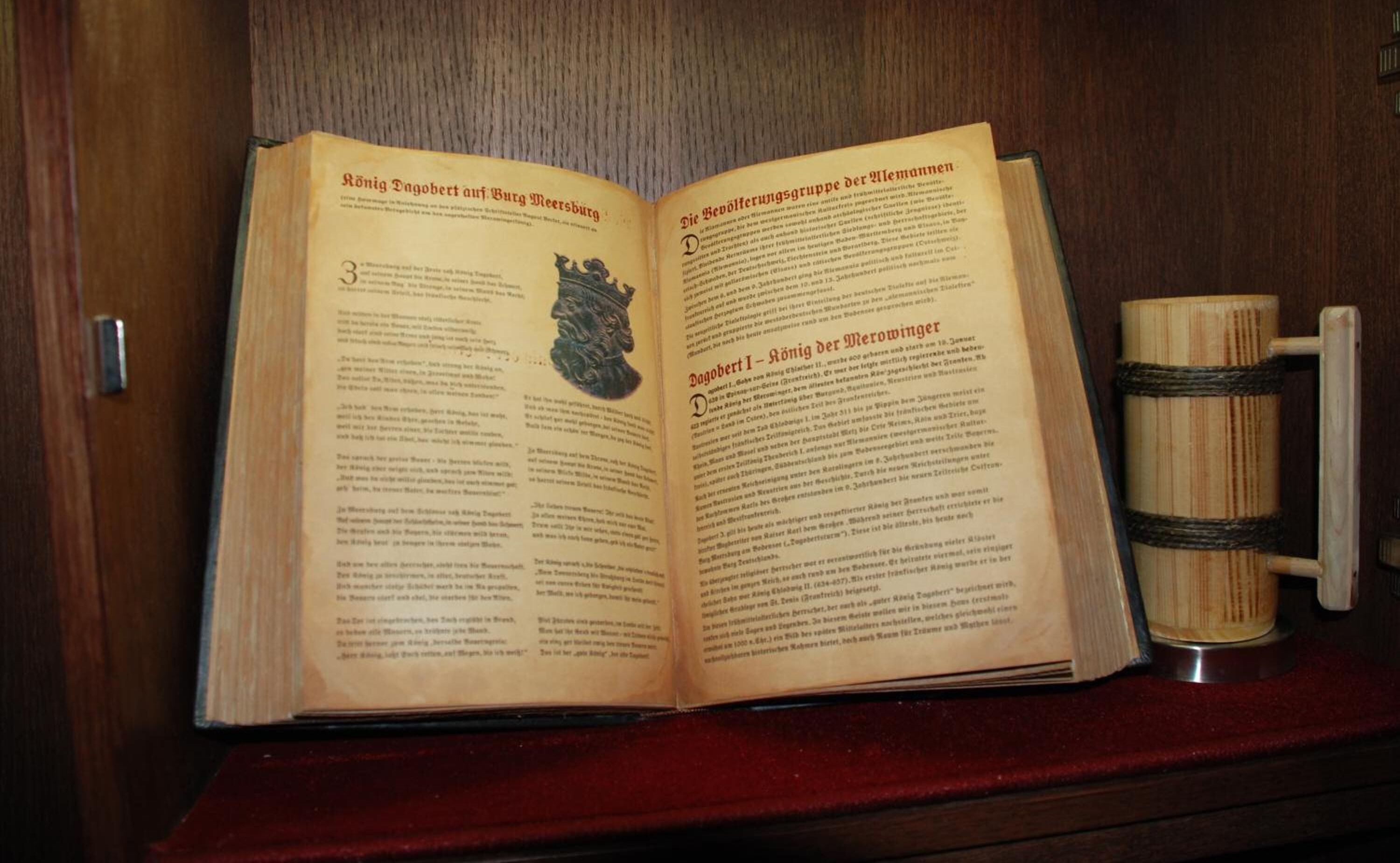 An open book with text and a wooden mug on a shelf.