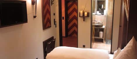 A hotel room with a bed, a television, a mirror, and a bathroom visible through an open door.