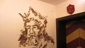 A wall with a textured portrait, a shelf with candles, and a door with a geometric pattern. - Mittelalterhotel-Gästehaus Rauchfang (Meersburg)